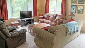 A living room with a television, leather sofas, a coffee table, and a fireplace. - Relaxing Getaway on Mt Hood - Right on the River! (Mount Hood Village)