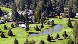 An aerial view of a golf course with a pond, surrounded by dense forest and residential buildings. - Relaxing Getaway on Mt Hood - Right on the River! (Mount Hood Village)