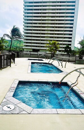 Zona de piscina con dos piscinas, un edificio de gran altura al fondo y un paseo marítimo cercado.
