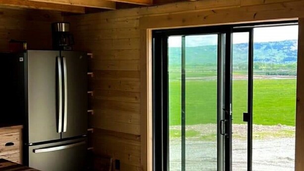 A kitchen with a large refrigerator and a sliding glass door leading to a grassy outdoor area. - Kia'a'yo Bear Cabin -- Modern Cabin -- 15 Min to Glacier East Entrance (Babb)