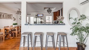 A kitchen with a central island, bar stools, a dining area with wooden furniture, and a potted plant.