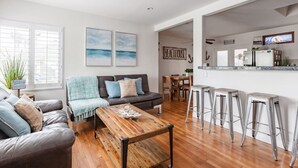 A modern living room with a dark leather sofa, a wooden coffee table, and a dining area with a wooden table and bar stools.
