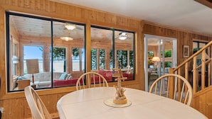 L’intérieur d’un chalet en bois, avec de grandes fenêtres, une table à manger et un escalier.