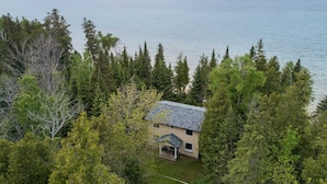 Une maison à deux étages, entourée d’une forêt dense, qui offre une vue sur une vaste étendue d’eau.