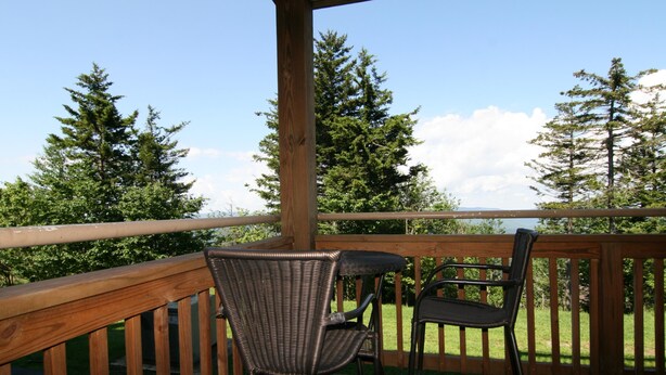 Een houten terras met twee rieten stoelen en een tafel, met uitzicht op een grasveld met bomen.