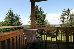 A wooden deck with two wicker chairs and a table, overlooking a grassy area with trees.