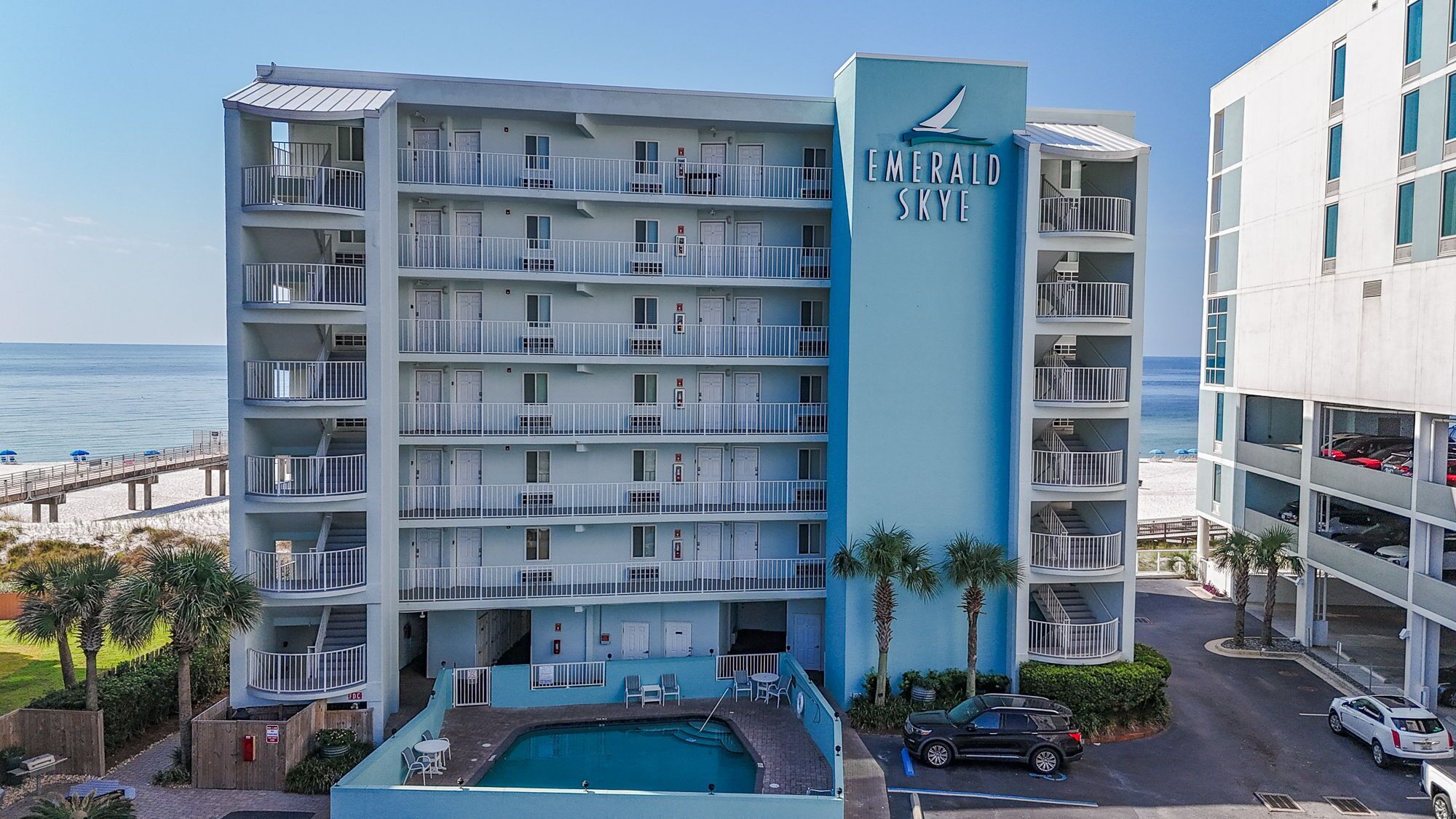 Un hotel de varios pisos con piscina, balcones y vista a la playa.