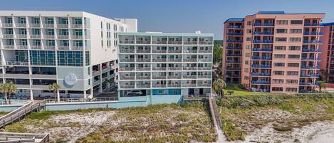 A beachfront hotel with multiple floors, balconies, and a pool area.