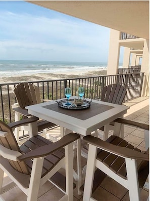 A balcony with a table and chairs overlooking the beach.