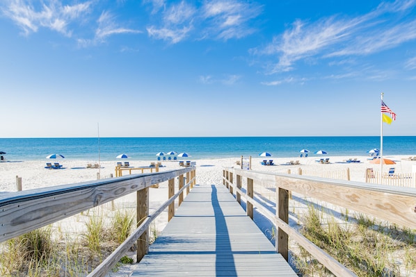 A wooden boardwalk leading to a beach with umbrellas and lounge chairs.