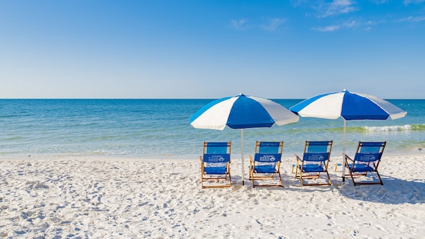 Une plage avec quatre chaises de plage bleues et blanches, placées sous des parasols assortis, toutes orientées vers l’océan.