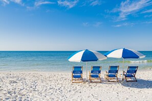 A beach with four blue and white beach chairs under matching umbrellas, facing the ocean.