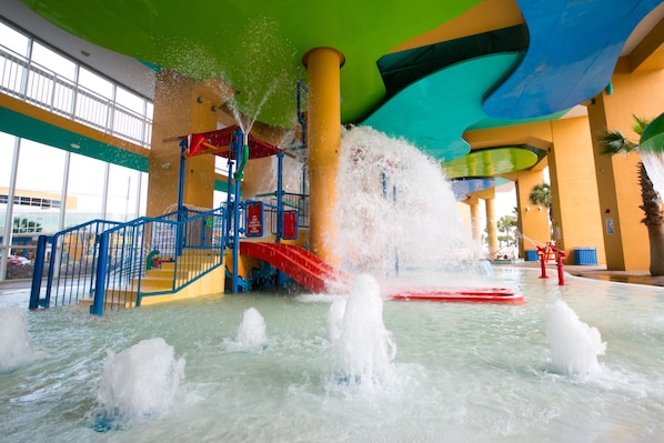 Ein Wasserpark mit einer roten Rutsche, mehreren Wasserstrahlen und einer farbenfrohen Decke.