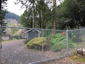 A chain-link fence with a small shed and a rock covered in moss. - Fish, hunt or relax - Riverfront Cozy 2bd Cabin on Umpqua River fenced 1.5 acres (Scottsburg)