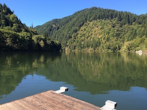 A wooden dock extending into a calm lake with dense forested hills in the background. - Fish, hunt or relax - Riverfront Cozy 2bd Cabin on Umpqua River fenced 1.5 acres (Scottsburg)