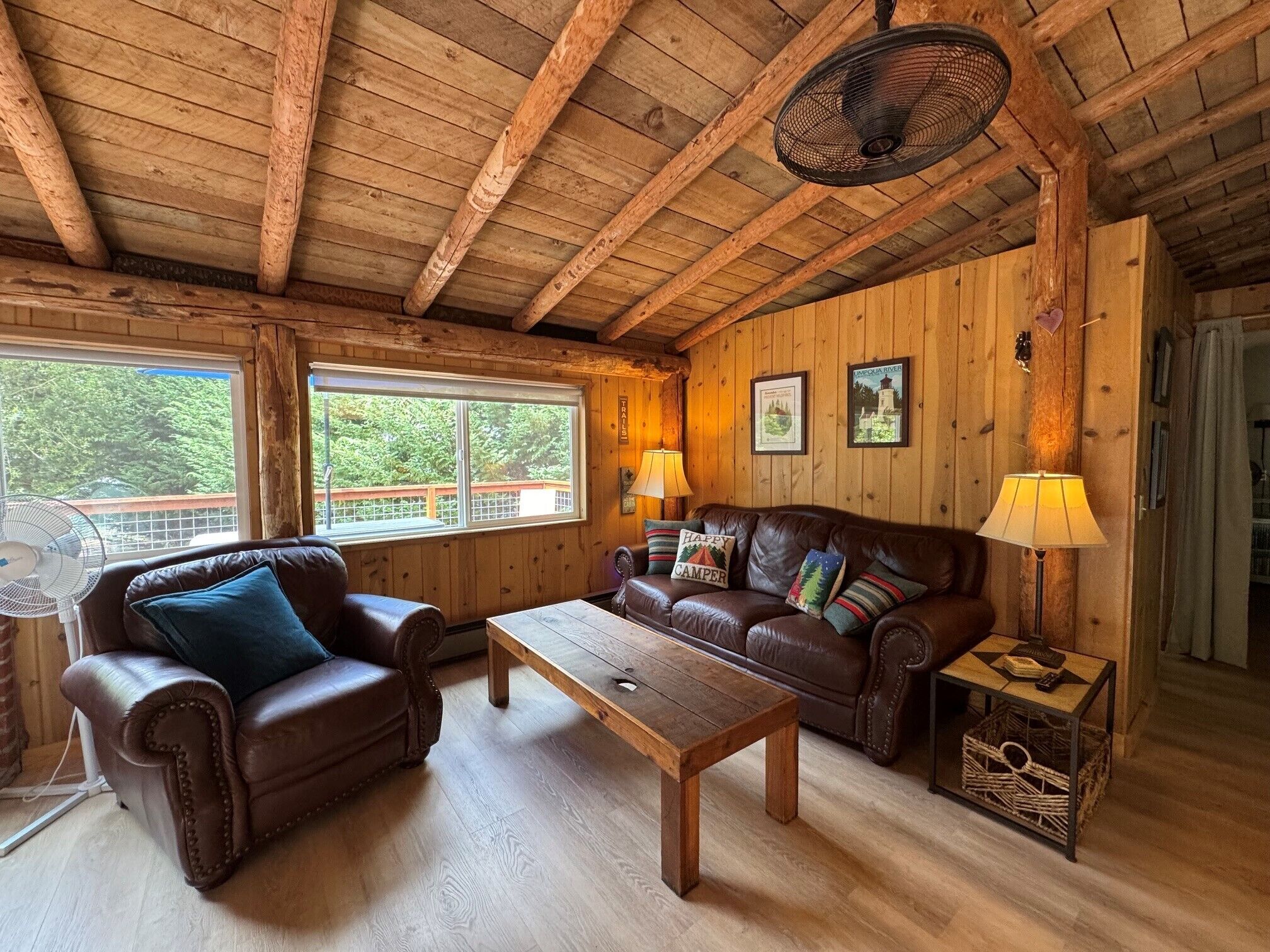 A cozy cabin interior with a wooden ceiling, a leather sofa, a wooden coffee table, and a fan.