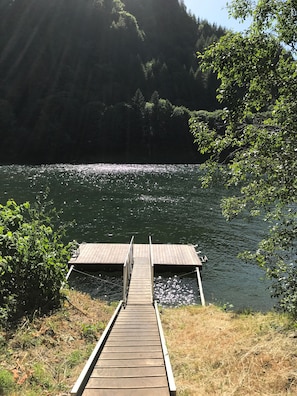 A wooden dock extending into a calm lake surrounded by dense forest. - Fish, hunt or relax - Riverfront Cozy 2bd Cabin on Umpqua River fenced 1.5 acres (Scottsburg)