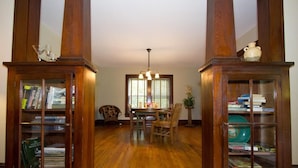 A wooden-paneled library with bookshelves, a dining table with chairs, and a chandelier.