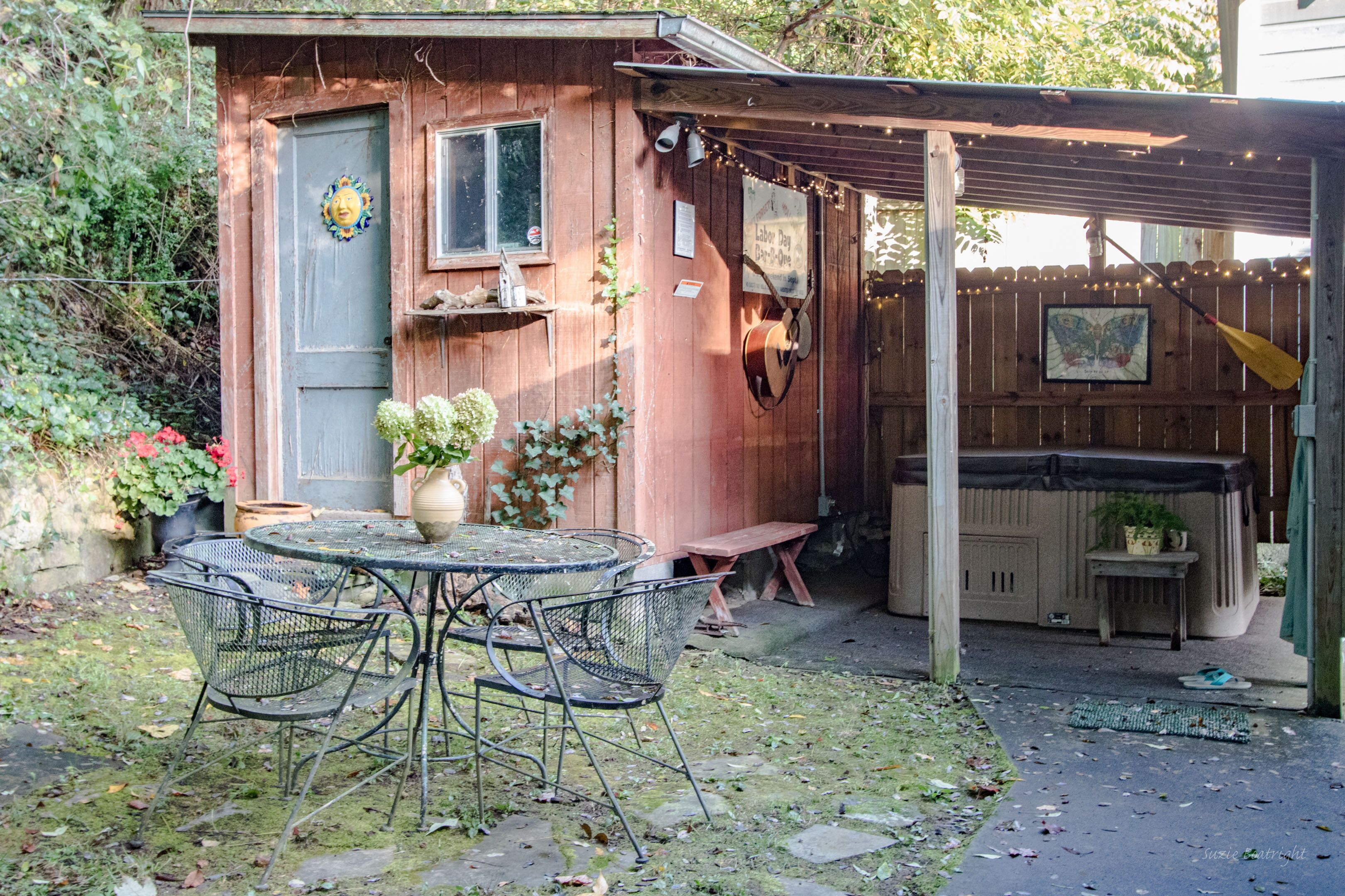 A wooden shed with a door, a small table with chairs, and a bench.