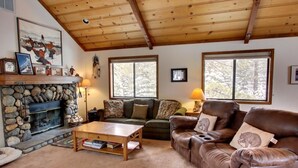 A cozy living room with a stone fireplace, leather sofas, and large windows. - Family-Friendly, Pet-Friendly, Tree-Surrounded Tahoe City Vacation Home (Tahoe City)