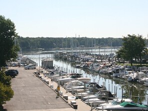 A marina with numerous boats docked along the water, a parking area with cars, and a clear view of the water.