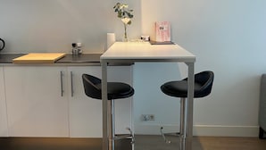 Een moderne keuken met een wit aanrecht, twee zwarte barkrukken, een vaas met bloemen en een roze notitieboekje op het aanrecht.