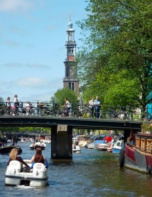 Un canal avec des bateaux, un pont avec des cyclistes et une tour en arrière-plan.