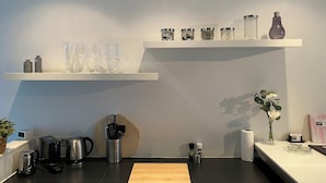 A modern kitchen with a wooden countertop, coffee makers, a kettle, and a hanging basket.