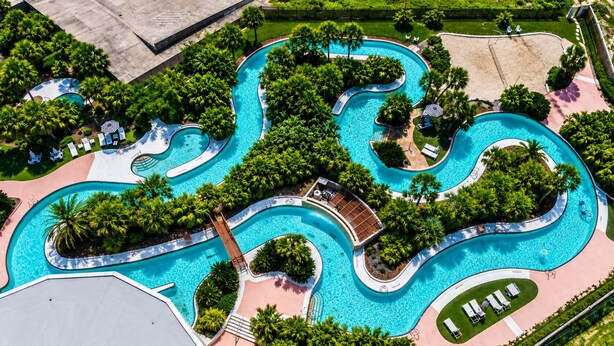 Vue aérienne d’un complexe hôtelier doté de plusieurs piscines, de palmiers et d’une plage.