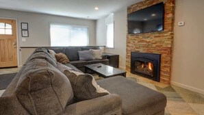 A modern living room with a sectional sofa, a fireplace, and a flat-screen TV mounted on a stone wall. - 1 Family Paradise, Den, Playground, Space (South Lake Tahoe)