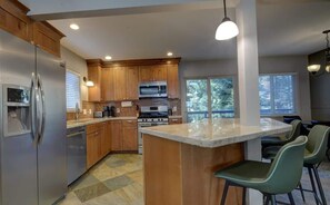 A modern kitchen with wooden cabinets, stainless steel appliances, and a central island with bar stools. - 1 Family Paradise, Den, Playground, Space (South Lake Tahoe)
