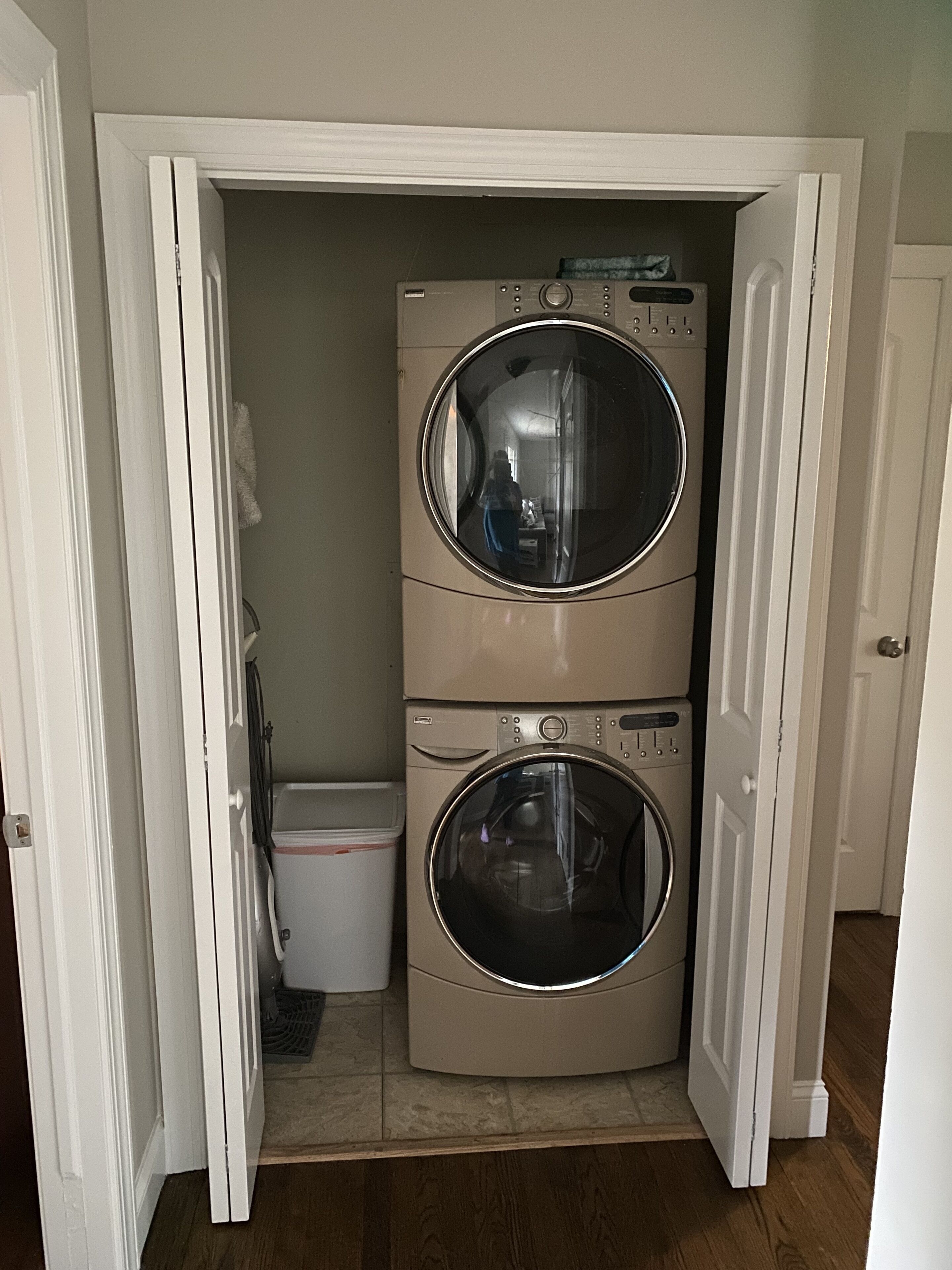A laundry room with two stacked front-loading washing machines and a small trash can.