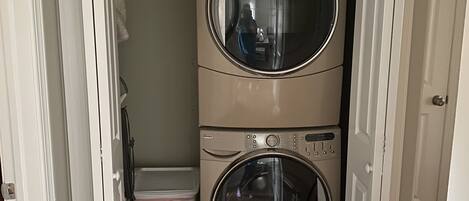 A laundry room with two stacked front-loading washing machines and a small trash can.
