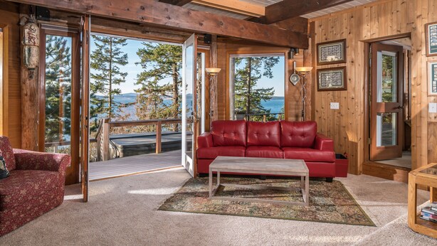 Interior acogedor de una cabaña con un sofá de cuero rojo, una mesa de centro de madera y vistas a un bosque y un lago a través de amplias ventanas.