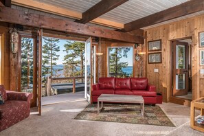 Ein gemütliches Blockhaus-Interieur mit einer roten Ledersofa, einem Holztisch und Blick auf einen Wald und See durch große Fenster.