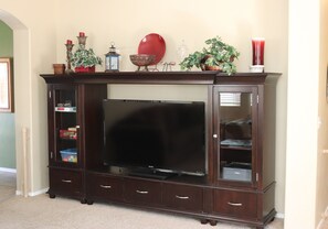 Eine dunkelholzausgekleidete Unterhaltungsanlage mit Flachbildfernseher, Schränken mit Glastüren und Dekorationselementen obenauf.