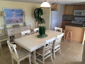 Una cocina con una isla central, muebles blancos y un comedor con sillas blancas.