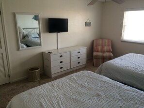 Un dormitorio con dos camas, televisión, cómoda, silla y ventana.