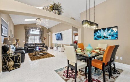 A spacious living room with a black leather sofa, a coffee table, and a dining area with a table set for four.