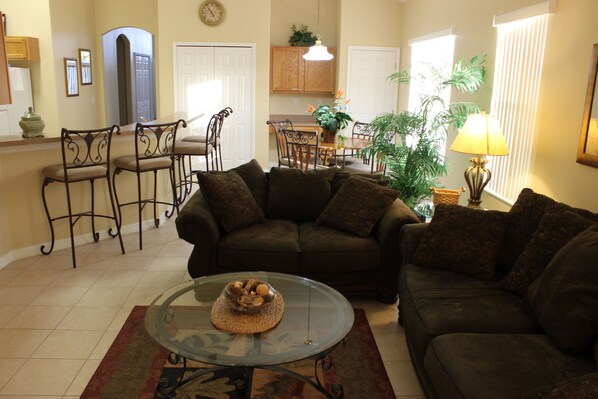 A living room with a glass coffee table, a dark brown sofa, and a dining area with wooden chairs and a table. - Dog friendly! Super Quiet, Pool, Close to Disney, Indoor Game Room, 2 Masters (Davenport)