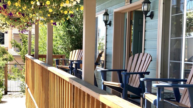 A wooden deck with Adirondack chairs, a wooden railing, and a hanging flower arrangement.