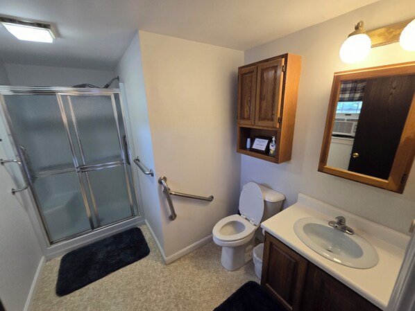 Un baño con cabina de ducha de vidrio, inodoro, lavabo y un mueble de madera sobre el lavabo.