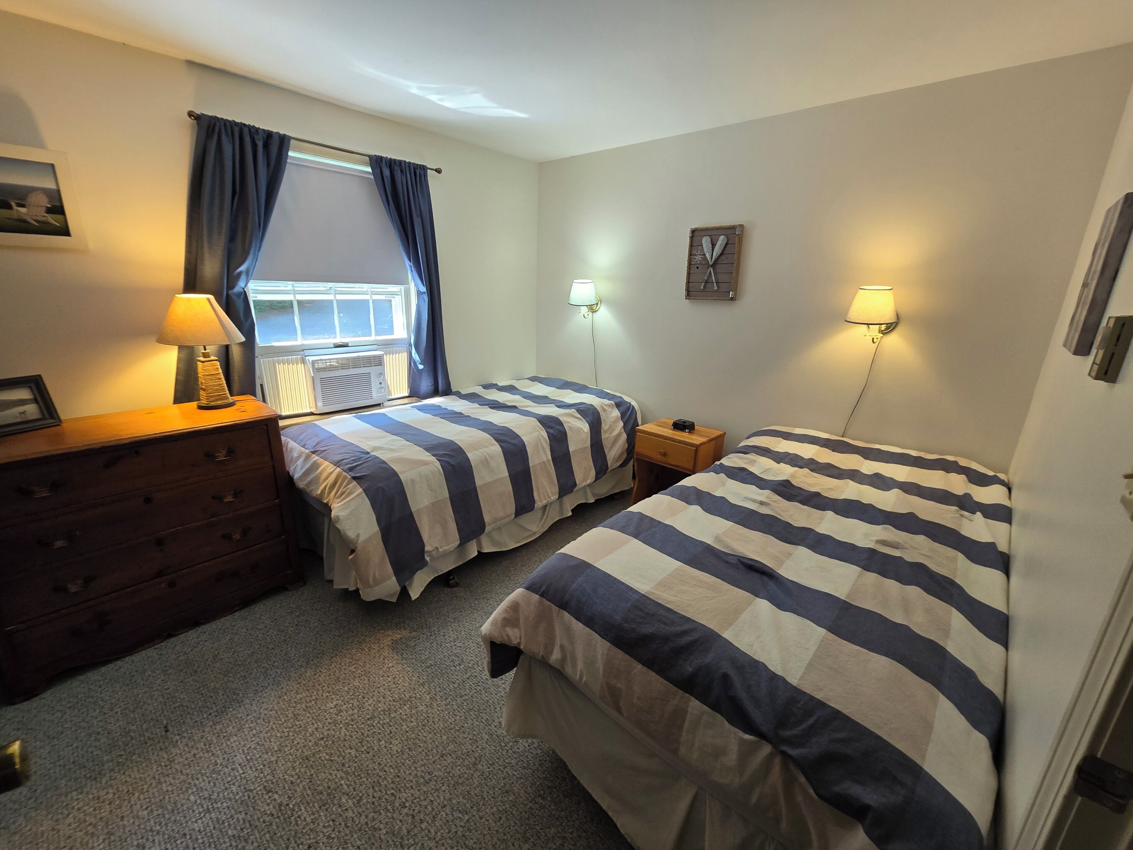 A bedroom with two beds, a dresser, a lamp, and a window with curtains.