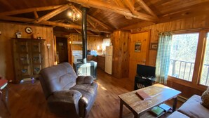 A wooden cabin interior with a sofa, a table, a television, and a kitchen area. - Secluded Mountain Cabin, Lakefront, Hiking, Fishing, Relaxing (Syria)