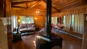 A cozy cabin interior with a wooden ceiling, a sofa, a table, and a fireplace. - Secluded Mountain Cabin, Lakefront, Hiking, Fishing, Relaxing (Syria)