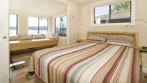 Una camera da letto con un letto grande, una panca integrata con cuscini, vista sull'esterno e una finestra che si affaccia sul cielo.