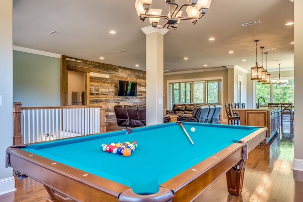 A pool table with balls, a stone wall, and a seating area with leather chairs.