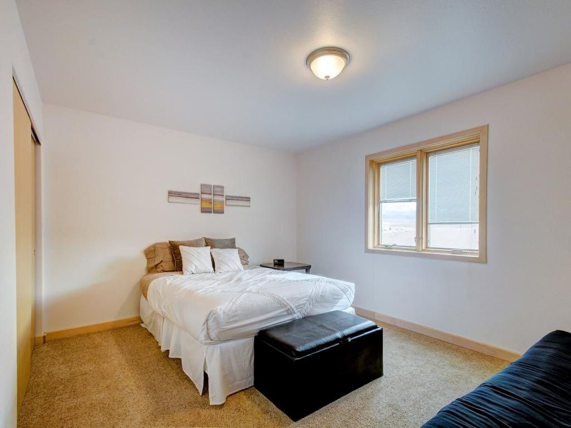 Una camera da letto con un letto, un comodino, una finestra e un punto luce a parete.