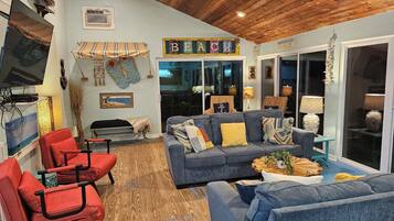 Un salon chaleureux avec un canapé bleu, des fauteuils rouges, un plafond en bois et une enseigne indiquant « Beach House ».