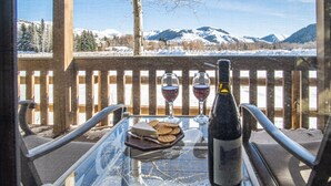 A glass table with a bottle and two glasses of red wine, a plate with crackers, and a view of snow-covered mountains. - SV137 - Walk to Lifts & Town - Hot Tub & Pool (Ketchum)